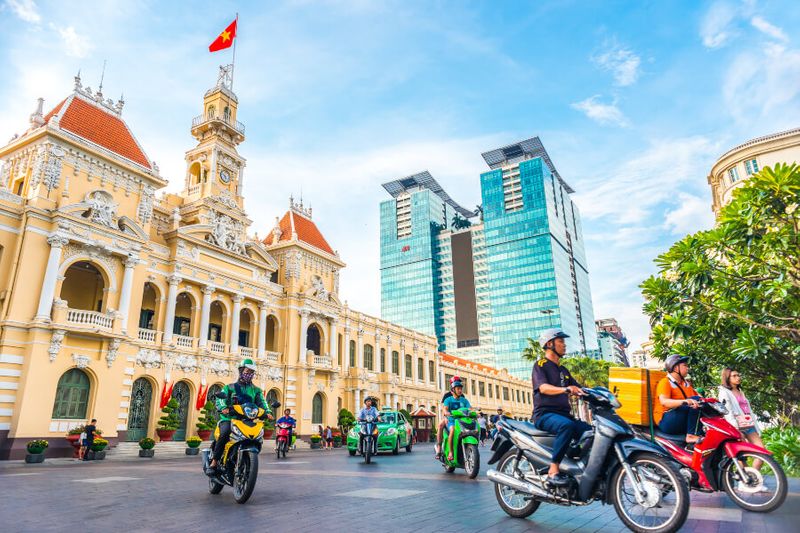 Downtown Saigon, with locals on motorcycles with the view of Saigon City Hall and the Vincom Center Towers.