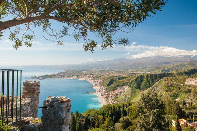 The village of Giardini Naxos and snowy Mount Etna seen from a viewpoint of the Roman Theatre in Taormina.