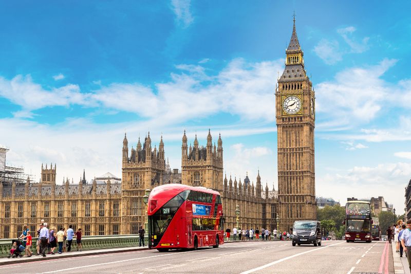 A typical London landscape with double decker busses and a view of the Big Ben.