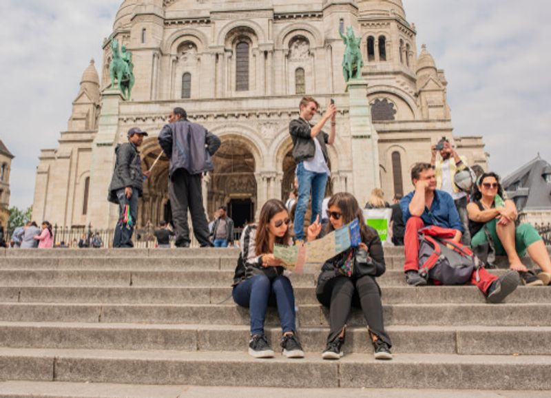 Tourists and locals alike gather on the steps of a grand building.