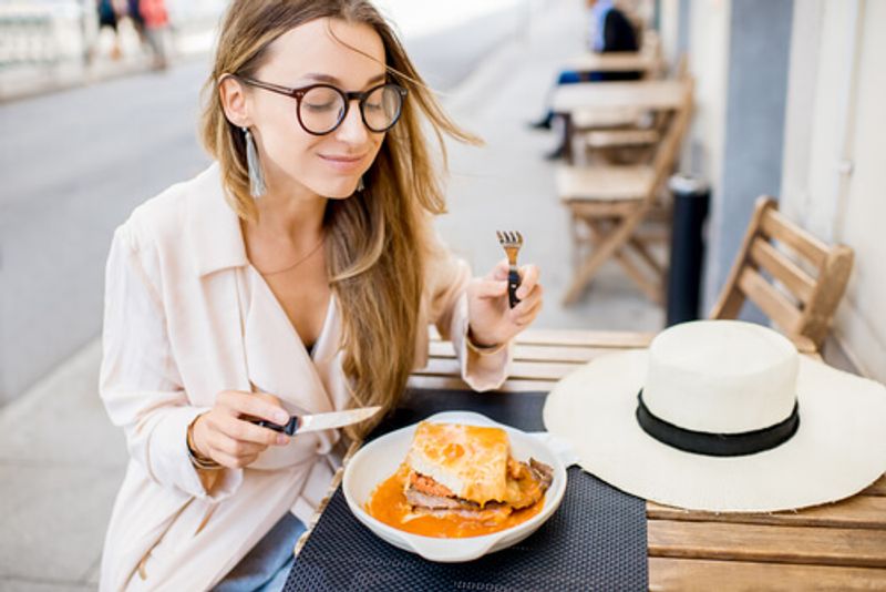 A woman enjoys a Francesinha Sandwich in Porto, Portugal.