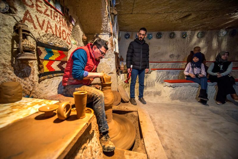 Tourists learn from a pottery master, exhibiting his skills.