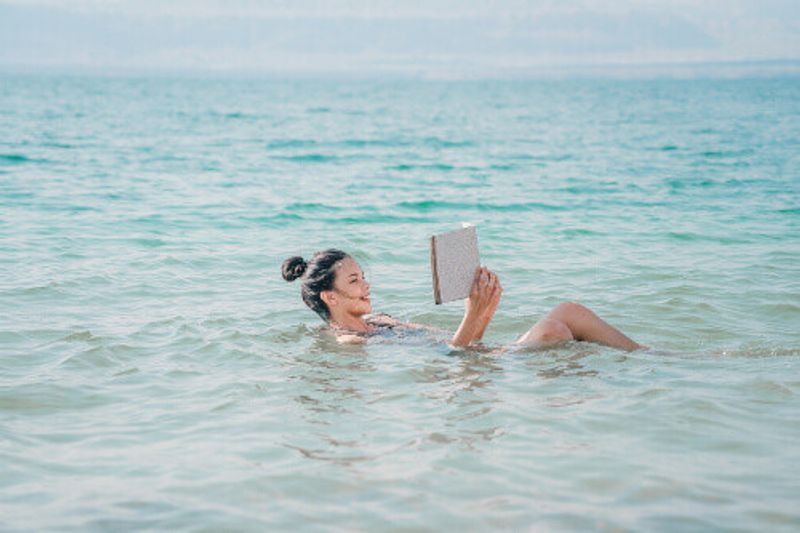 A young woman reads while floating on the surface of the Dead Sea, Jordan.