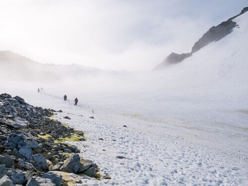 People hiking up and down snow slope of Spigot Peak in the mist at Graham Land in the Antarctic Peninsula, Antarctica.