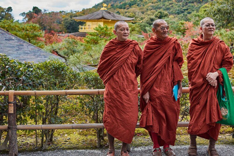 Buddhist monks stand in front of the Kinkakuji Temple or Golden Pavilion, a UNESCO world heritage site in Kyoto, Japan.