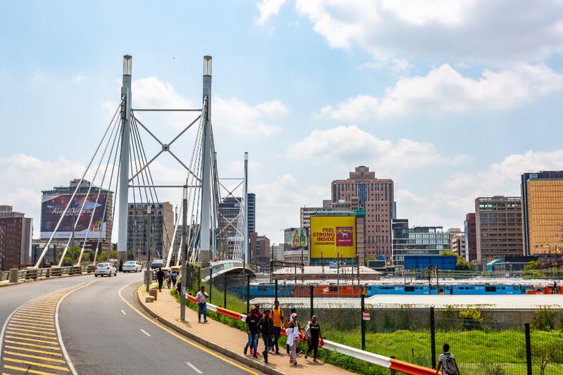 The Nelson Mandela Bridge is bustling with trains, cars and people passing by.