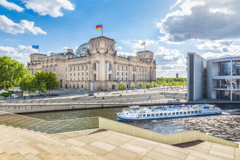 The Government district with an excursion boat on Spree river passing the famous Reichstag Building and Paul Lobe Haus in Berlin.