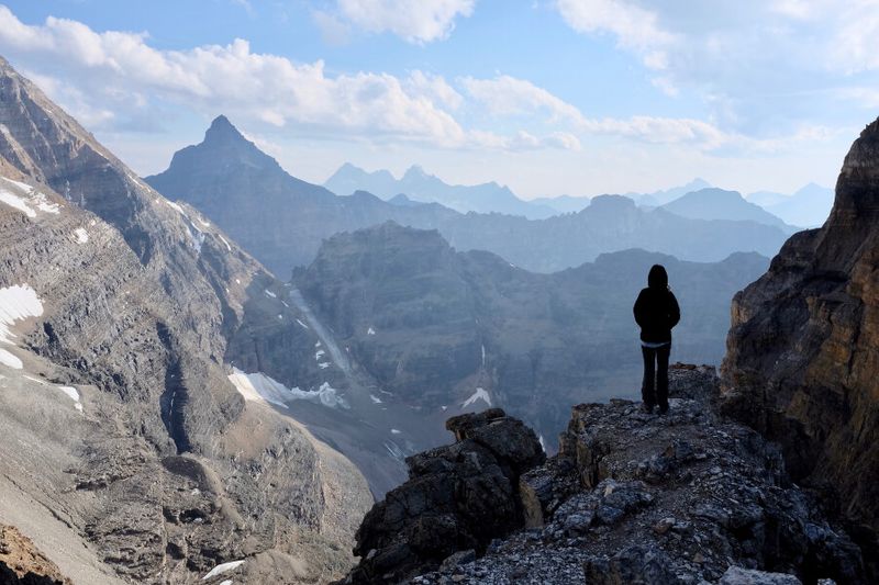 A hiker enjoys the view on the edge of Abbot Pass, overlooking Mount Lefroy.