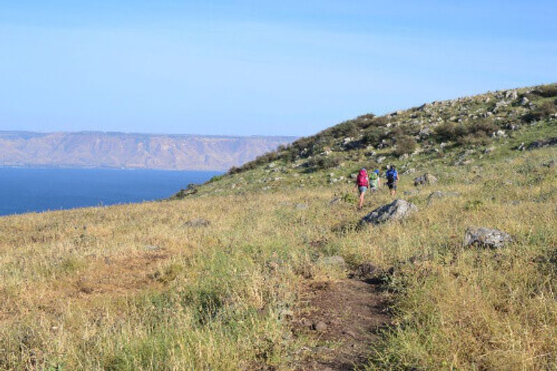 A group of hikers walk the Jesus Trail with a view of Mt. Arbel.