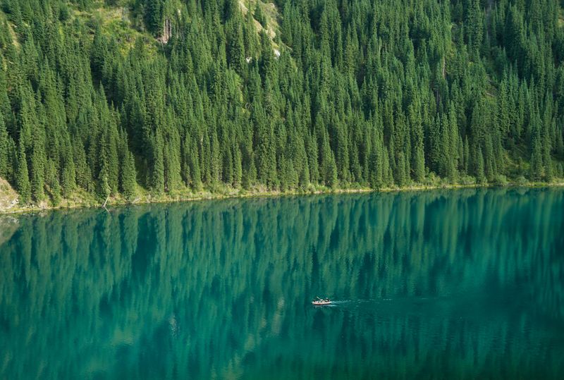 Wooden boat on Kolsai Lake surrounded by pine forest, a hidden gem in Kazakhstan nature. 