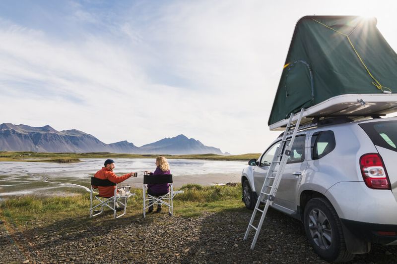 Young couple sitting on a folding chair next to a rented off road SUV with a tent.