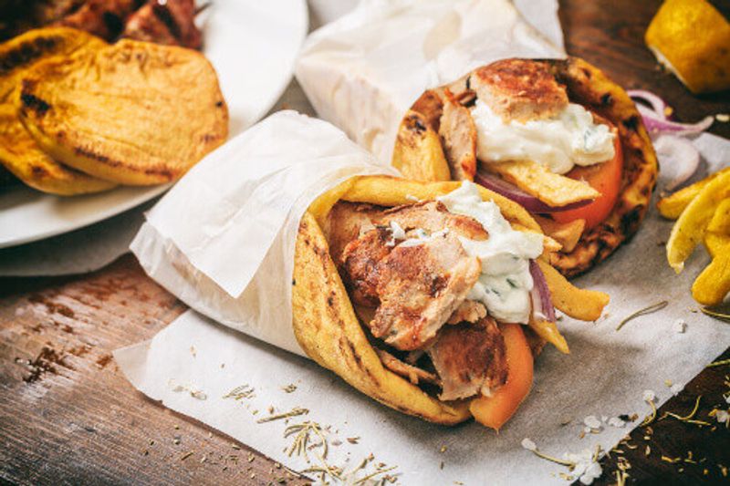 Greek Gyros Souvlaki, wrapped in a pita bread on a wooden background.