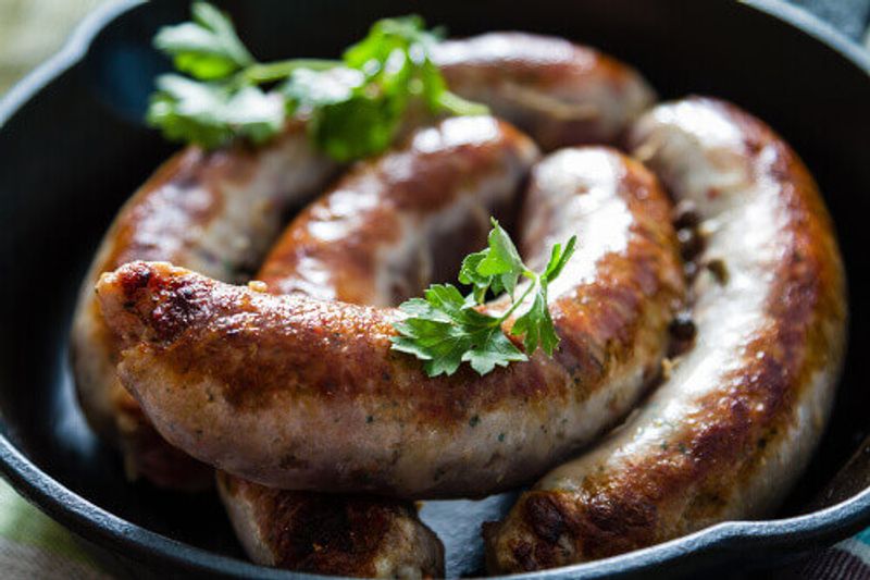 Grilled German sausages or, Bratwurst, on a pan with herbs and spices.