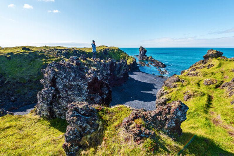 Woman on top of a lava rock observing the landscape of Djupalonssandur Beach in Snaefellsjokull National Park.