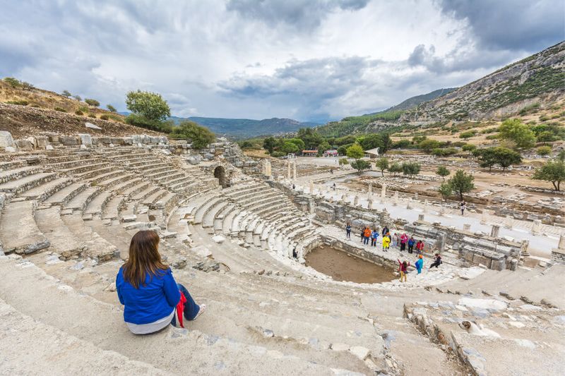 Tourists and a woman sitting at the ancient amphitheatre in Ephesus
