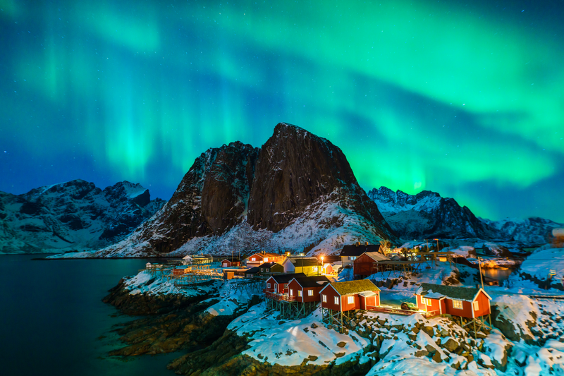 Snow-covered peaks and fjords of Norway’s Lofoten Islands glowing under the northern lights in January, the perfect winter destination for snowshoeing, igloo stays and Arctic scenery.