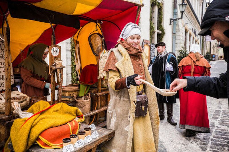 An Estonian woman dressed in the traditional medieval costume, handing tourists nuts.