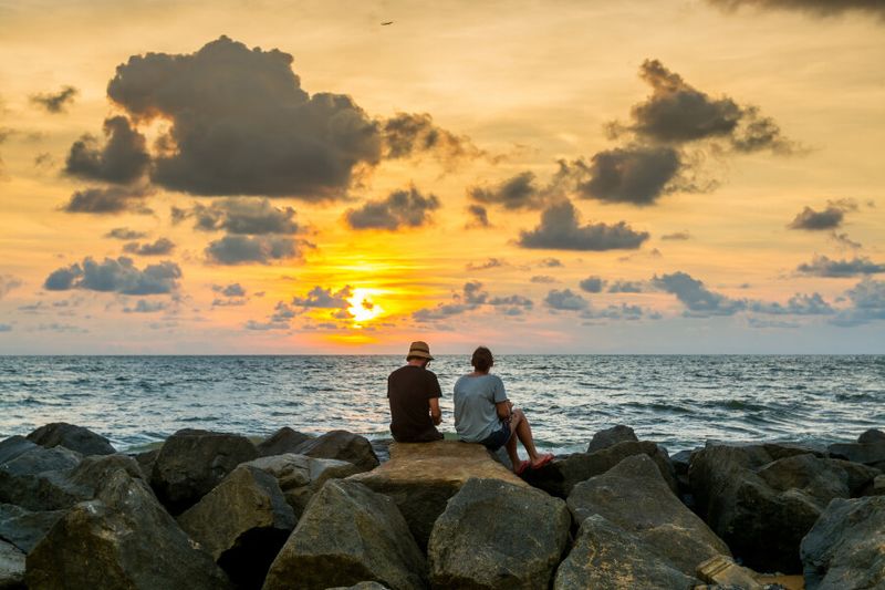 A couple sitting on the rocks sand watching the sunset in Negombo Beach.