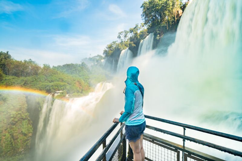 A woman stands close to Iguazu Falls, taking in the natural beauty.