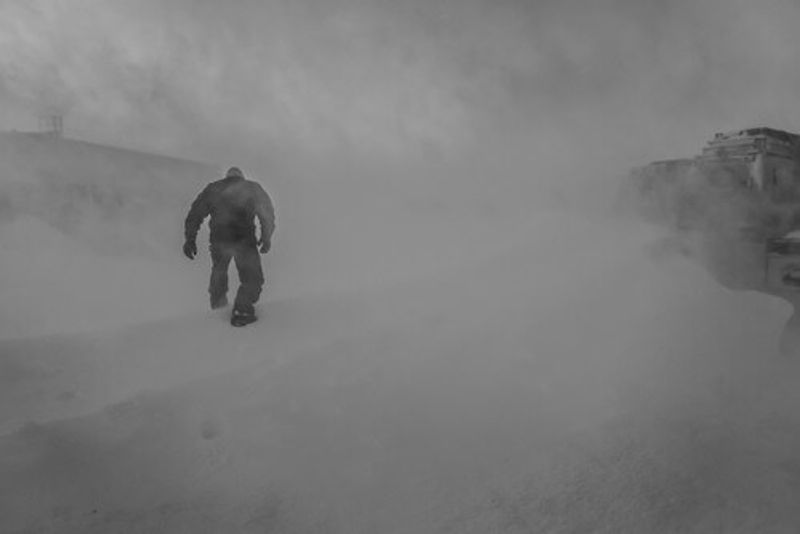 A lone Antarctic worker walks through a Blizzard in Antarctica.