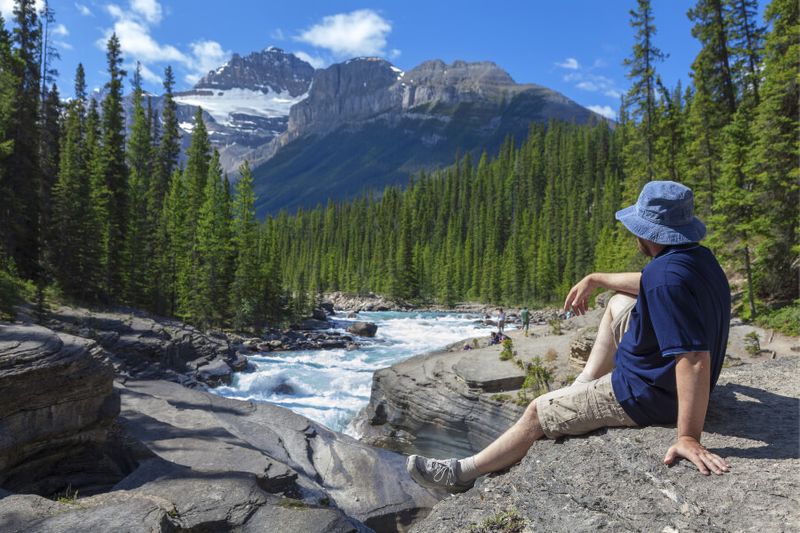 Tourist sitting at the edge of a canyon looking at the Canadian Rockies in Jasper National Park.