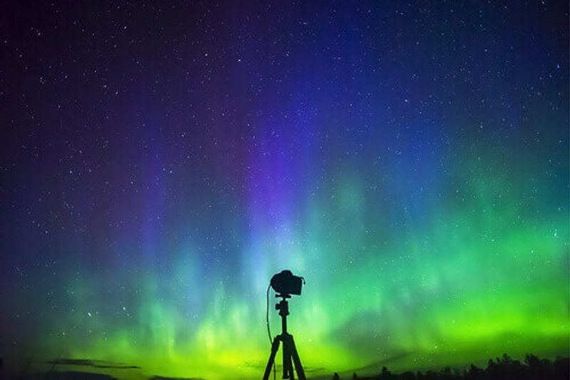 Silhouette of DSLR camera on tripod in front of a brilliant and vibrant Aurora Borealis in Norway.