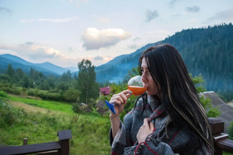 A young woman drinks golden champagne, against the background of the mountains.