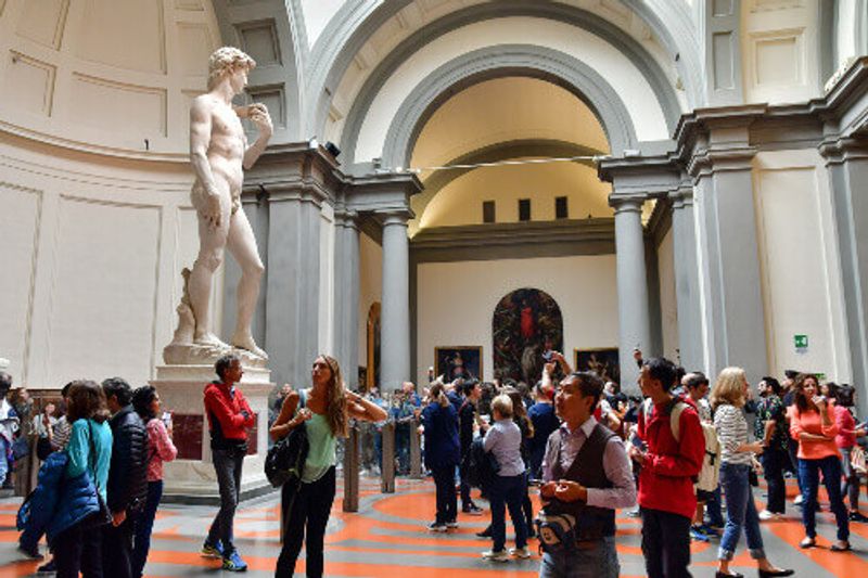 Tourists watch and photograph the statue of David.