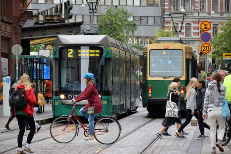 A woman on a bike crosses in front of a tram with others in the Old Town, Helsinki.