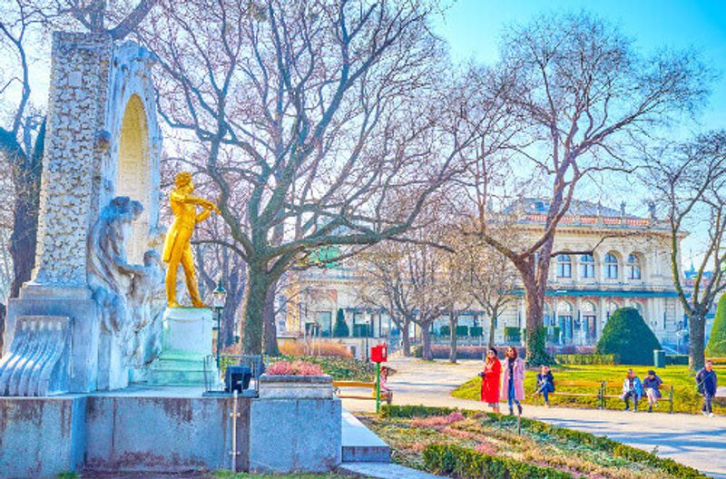 Group of tourists taking selfies and photos with the Golden Strauss Statue in the City Park, Vienna.