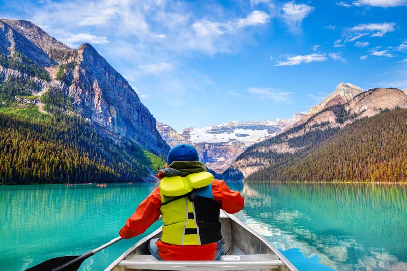 Tourists enjoy canoeing on Lake Louise with the view of Mount Victoria glacier.