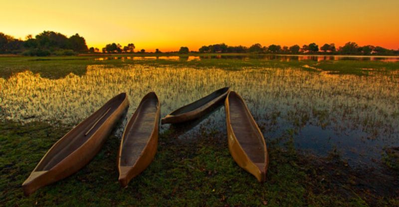 A traditional dugout canoe sits on the shore against the sunset.