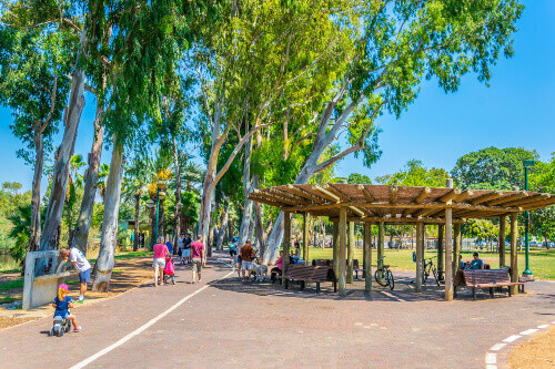 People are enjoying a sunny day of Shabbat at a promenade alongside the river in HaYarkon Park.